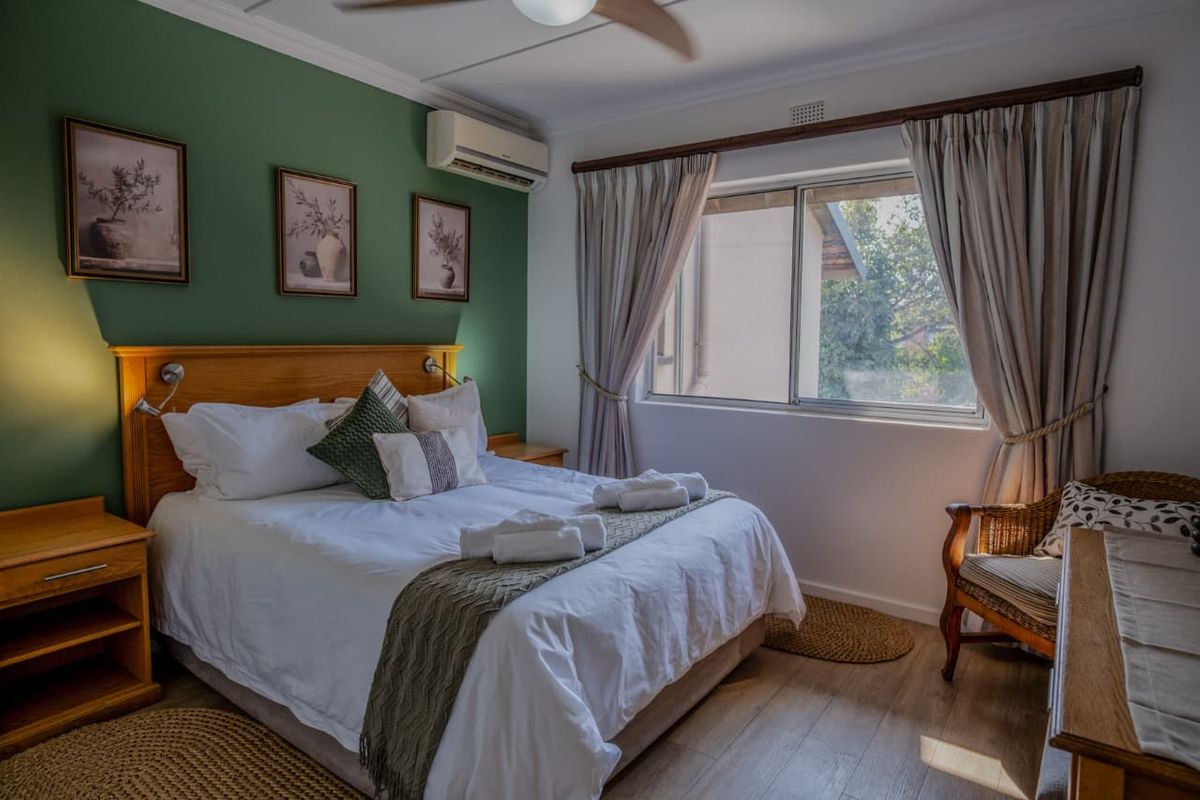 A well-maintained bedroom featuring laminate flooring, a ceiling fan, and a split-system air conditioner, with a large window providing natural light.
