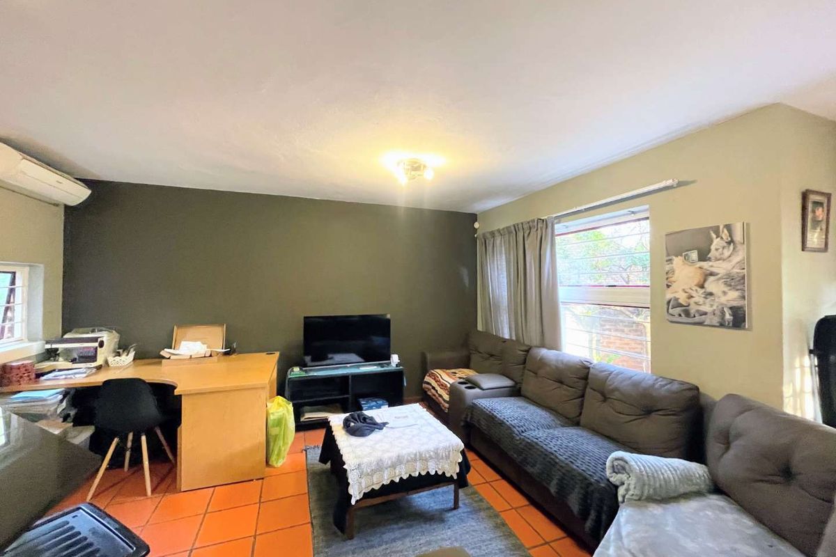 A living room featuring terracotta floor tiles, a wall-mounted air conditioning unit, and large windows allowing natural light into the space.