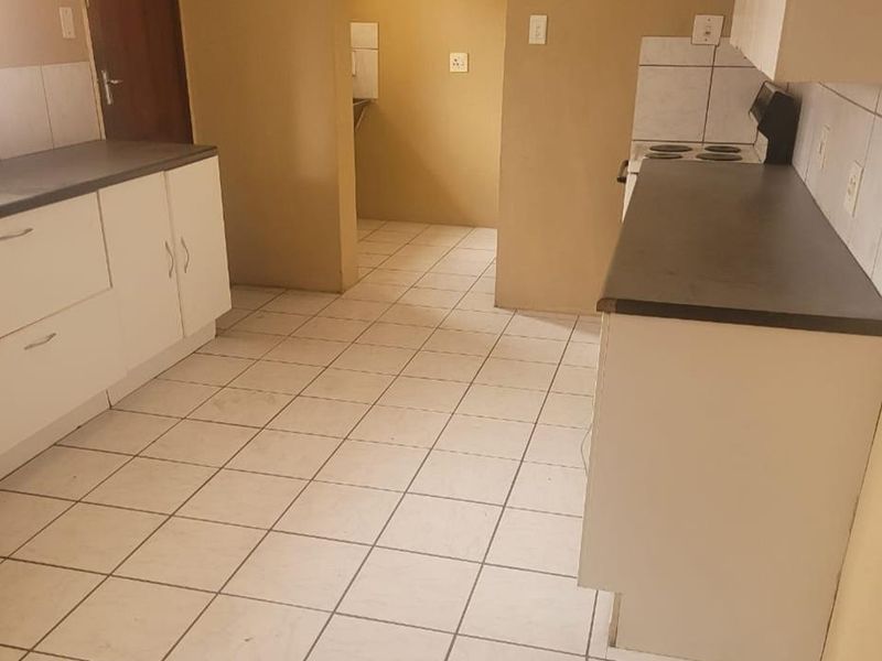 A functional kitchen featuring built-in cabinetry, laminate countertops, and tiled flooring, with an adjacent scullery area.