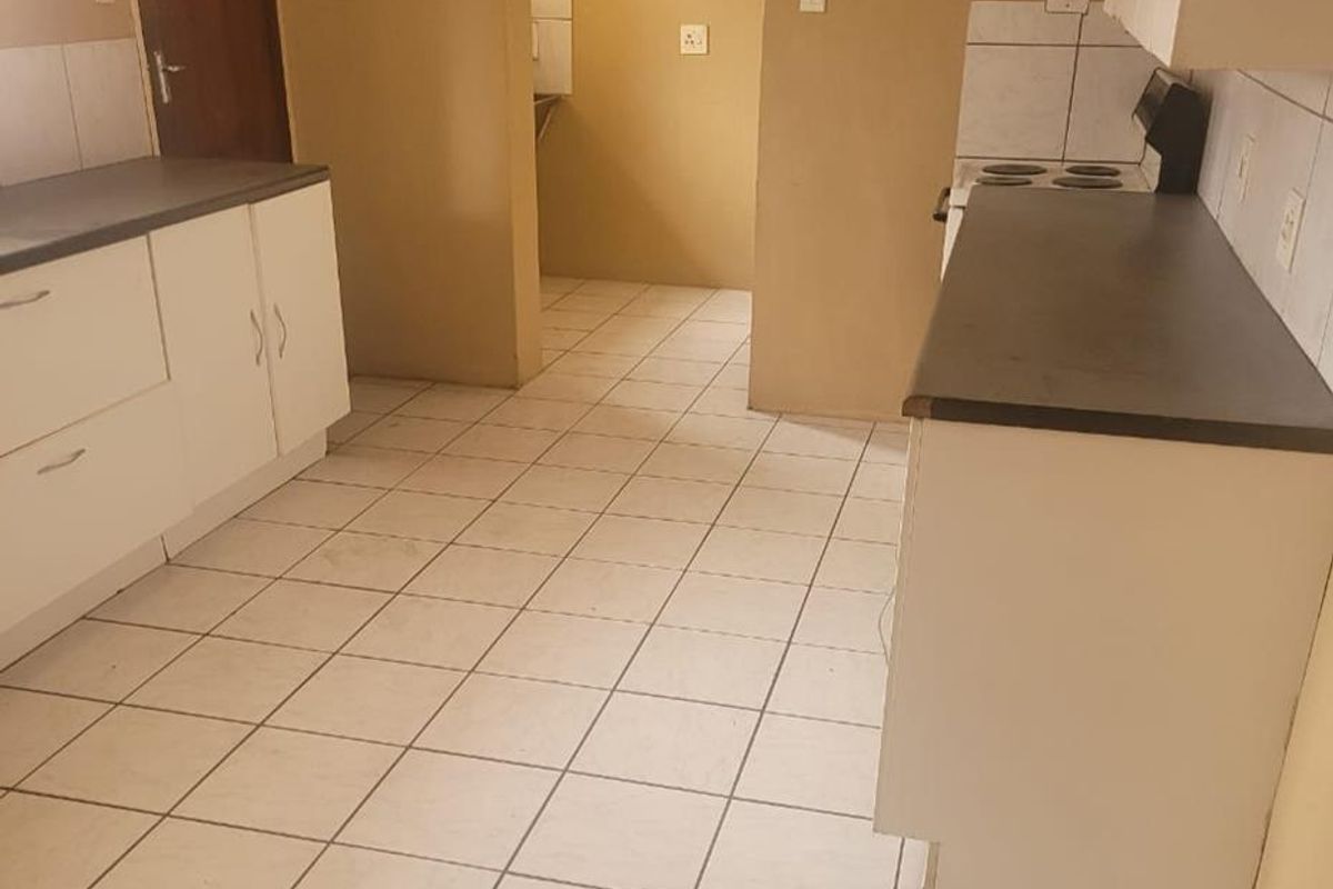 A functional kitchen featuring built-in cabinetry, laminate countertops, and tiled flooring, with an adjacent scullery area.