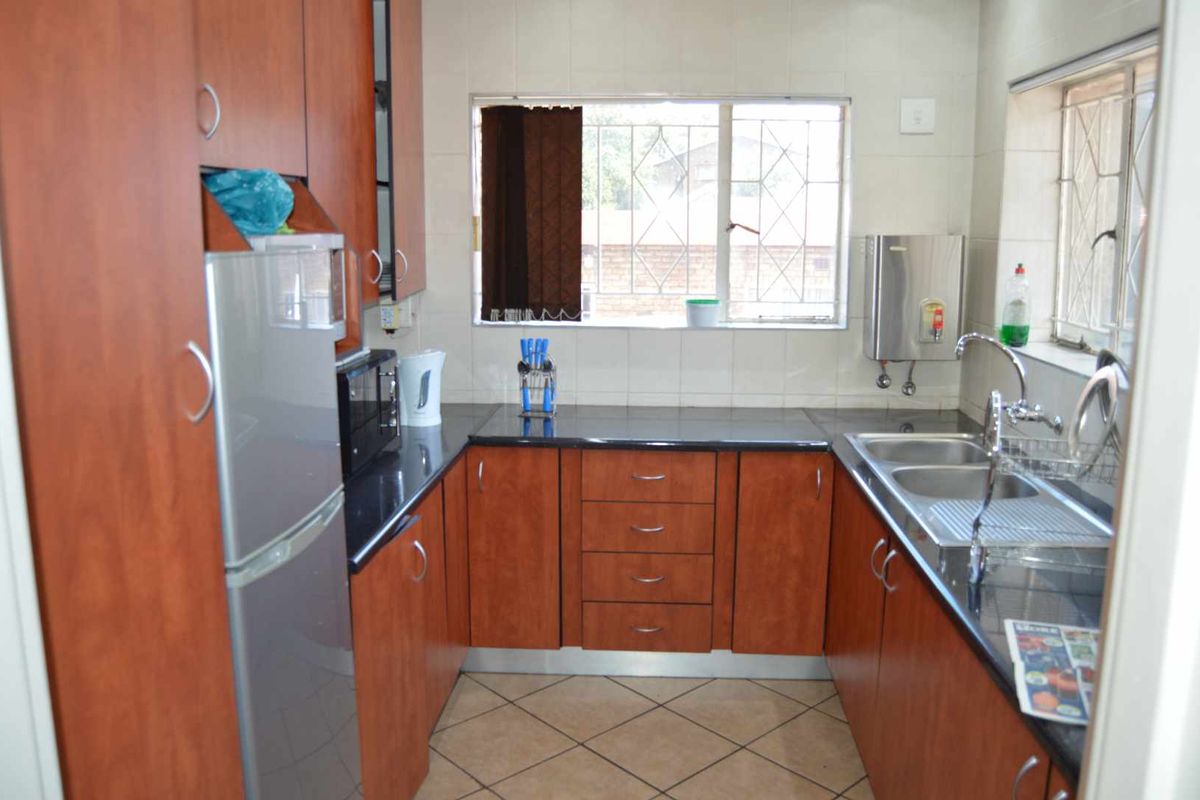 A functional kitchen featuring wood-finish cabinetry, dark granite countertops, a double stainless steel sink, and tiled flooring.