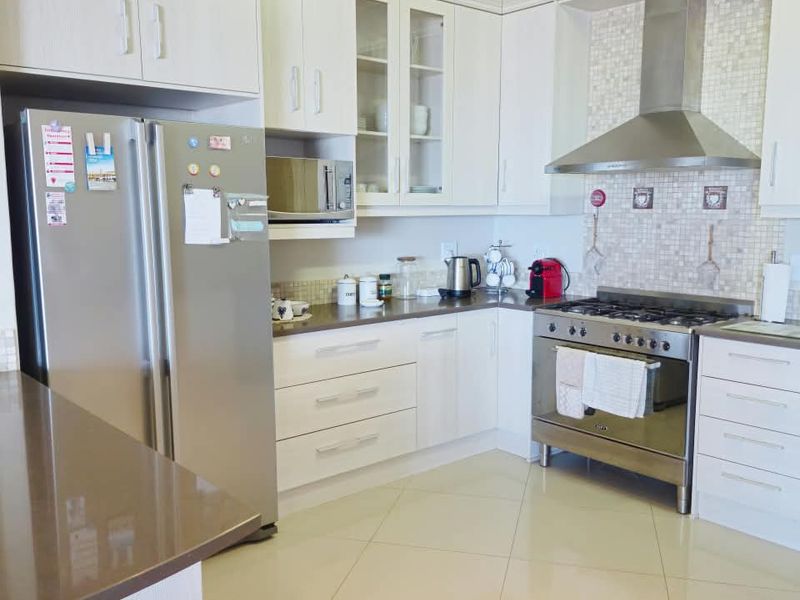 Modern kitchen featuring white cabinetry, stone countertops, stainless steel gas stove with extractor fan, and mosaic tile backsplash with polished floor tiles.