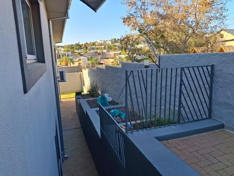 A side exterior view showing a paved walkway, retaining walls with integrated metal railings, and an external air conditioning unit.