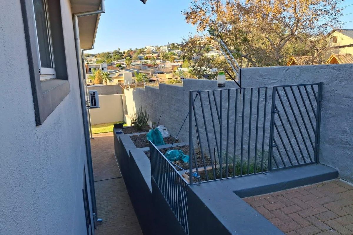 A side exterior view showing a paved walkway, retaining walls with integrated metal railings, and an external air conditioning unit.