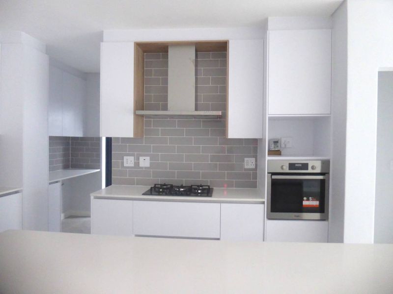 Modern kitchen featuring white handleless cabinetry, quartz countertops, a gas hob, built-in oven, and a stylish grey subway tile backsplash.