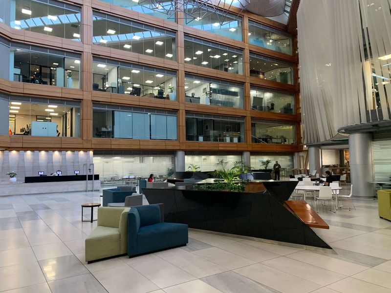 Spacious modern office atrium featuring a multi-level glass facade, polished tile flooring, and a central reception area with contemporary architectural design.
