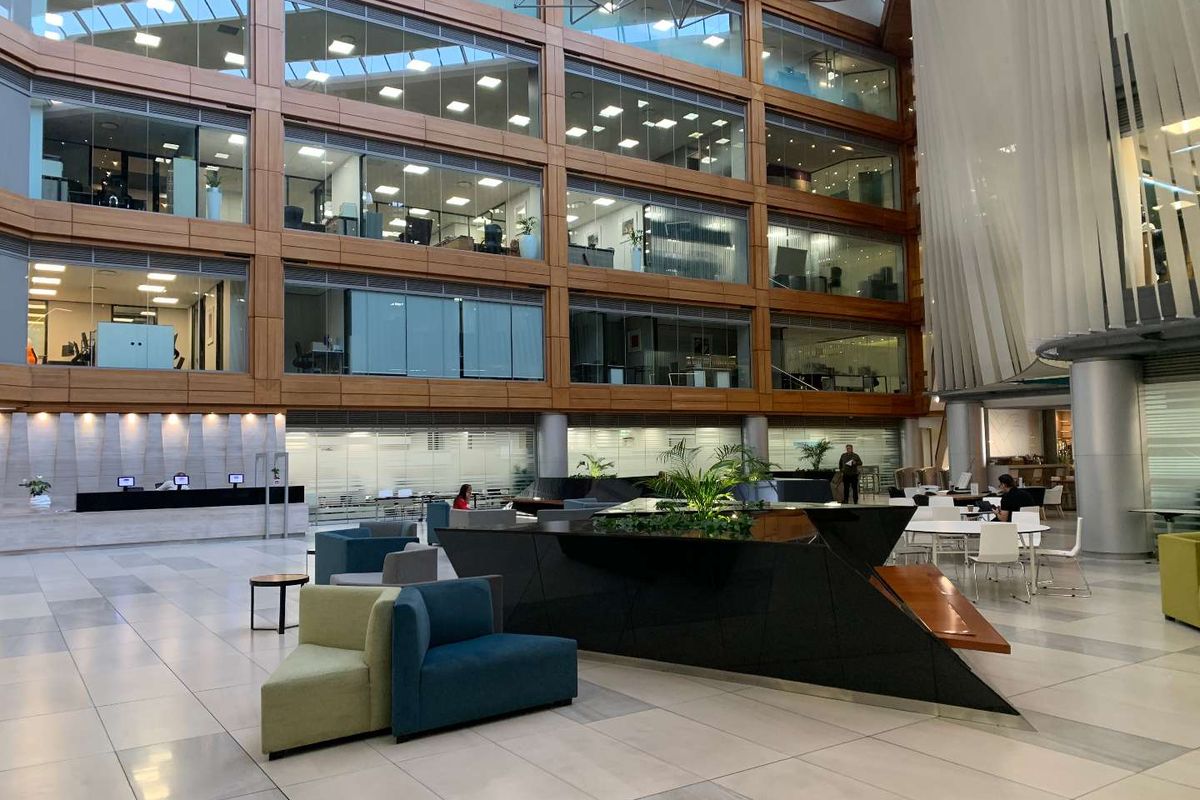 Spacious modern office atrium featuring a multi-level glass facade, polished tile flooring, and a central reception area with contemporary architectural design.