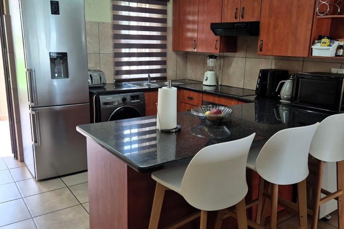 A functional kitchen featuring dark wood cabinetry, granite countertops, a breakfast bar, and tiled flooring, with some visible wear on the wall finishes.