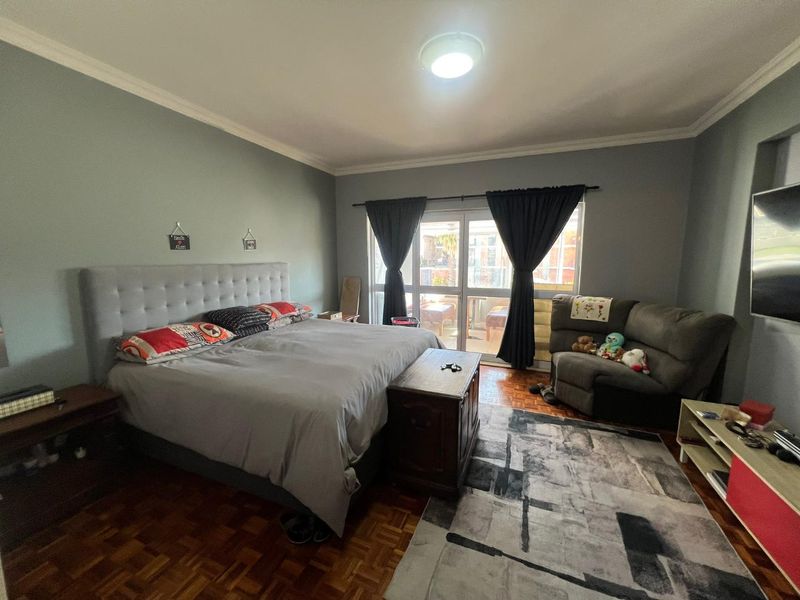 Spacious bedroom featuring classic parquet flooring, coved ceilings, and a sliding glass door providing access to an outdoor balcony area.