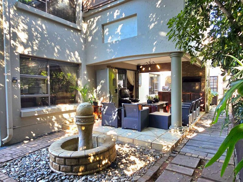 A covered patio area featuring a stone fountain, paved flooring, and a structural column, providing a pleasant outdoor living space.