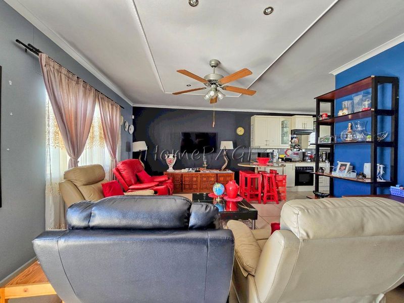 Open-plan living and kitchen area featuring tiled floors, a ceiling fan, and built-in kitchen cabinetry with integrated appliances.