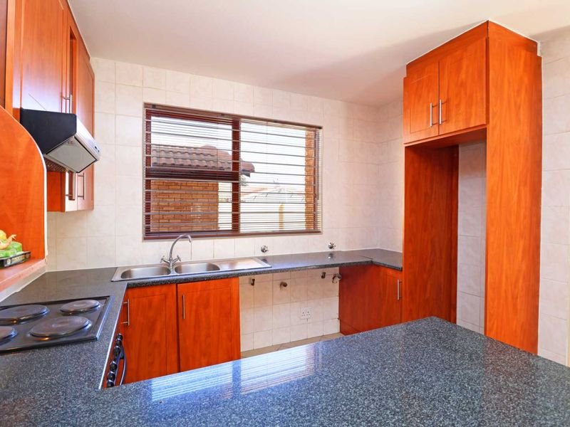 A functional kitchen featuring wood-finish cabinetry, granite countertops, a double sink, and a built-in electric hob with an extractor fan.