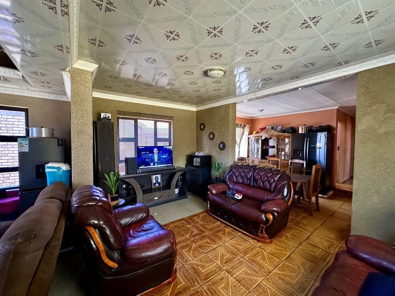 Open-plan living and dining area featuring tiled flooring and decorative ceiling tiles, offering a functional layout with integrated kitchen access.
