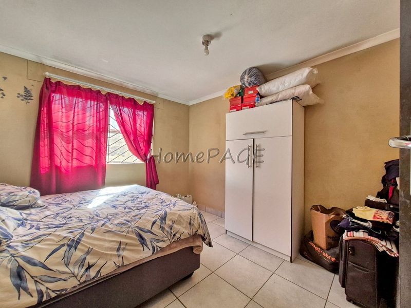 A bedroom featuring tiled flooring and a window with security bars, requiring cosmetic updates to the wall finishes.