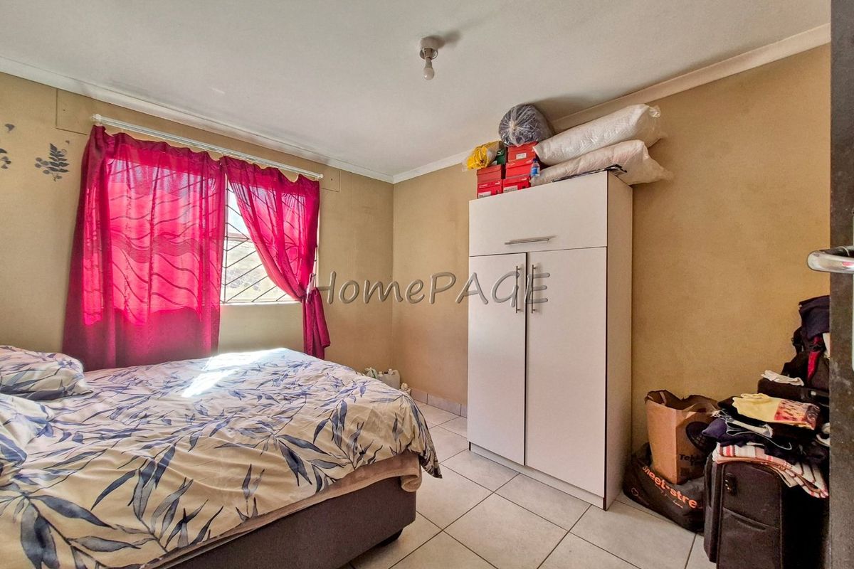 A bedroom featuring tiled flooring and a window with security bars, requiring cosmetic updates to the wall finishes.