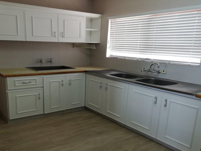 A clean, functional kitchen featuring white cabinetry, dual sink areas, laminate countertops, and light wood-look flooring with natural light from a window.