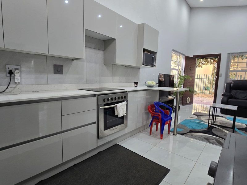 Modern open-plan kitchen featuring high-gloss cabinetry, stone countertops, and integrated appliances, flowing directly into the living area with access to the exterior.