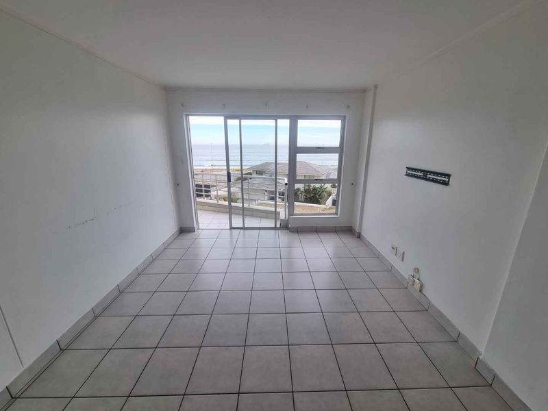 An empty living room featuring tiled flooring and a sliding glass door that opens to a balcony with ocean views.