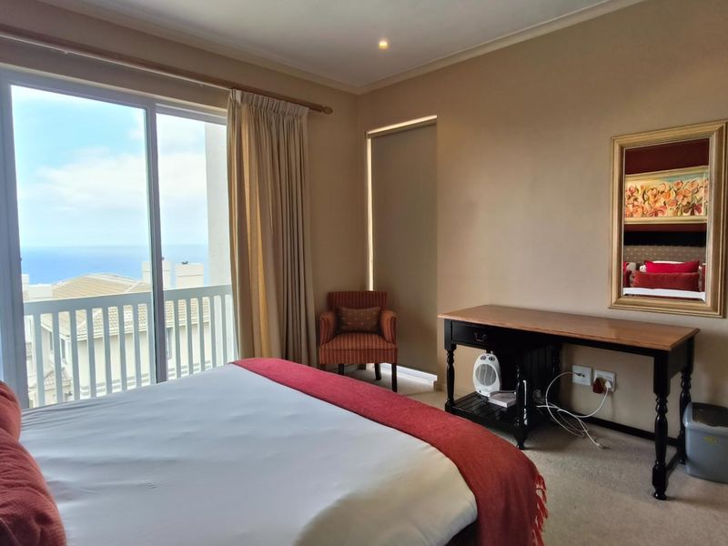 A well-lit bedroom featuring carpeted flooring, recessed lighting, and a large sliding glass door providing access to a balcony with coastal views.