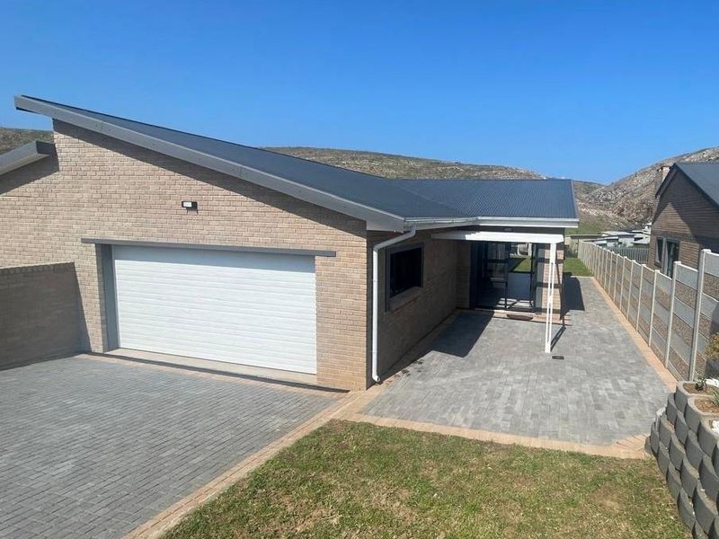 Modern single-story brick home featuring a paved driveway, sectional garage door, and a covered entrance, set against a scenic hillside backdrop.