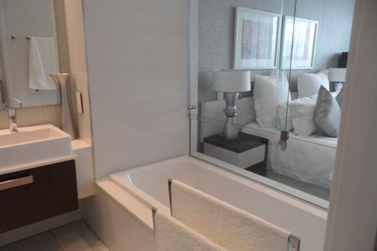 Modern bathroom featuring a built-in bathtub, wall-mounted vanity with basin, and a glass partition wall looking into the adjacent bedroom.