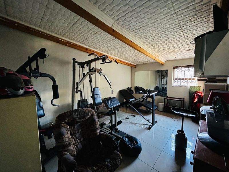 A dedicated home gym space featuring tiled flooring, a textured ceiling with exposed timber beams, and a wall-mounted mirror.