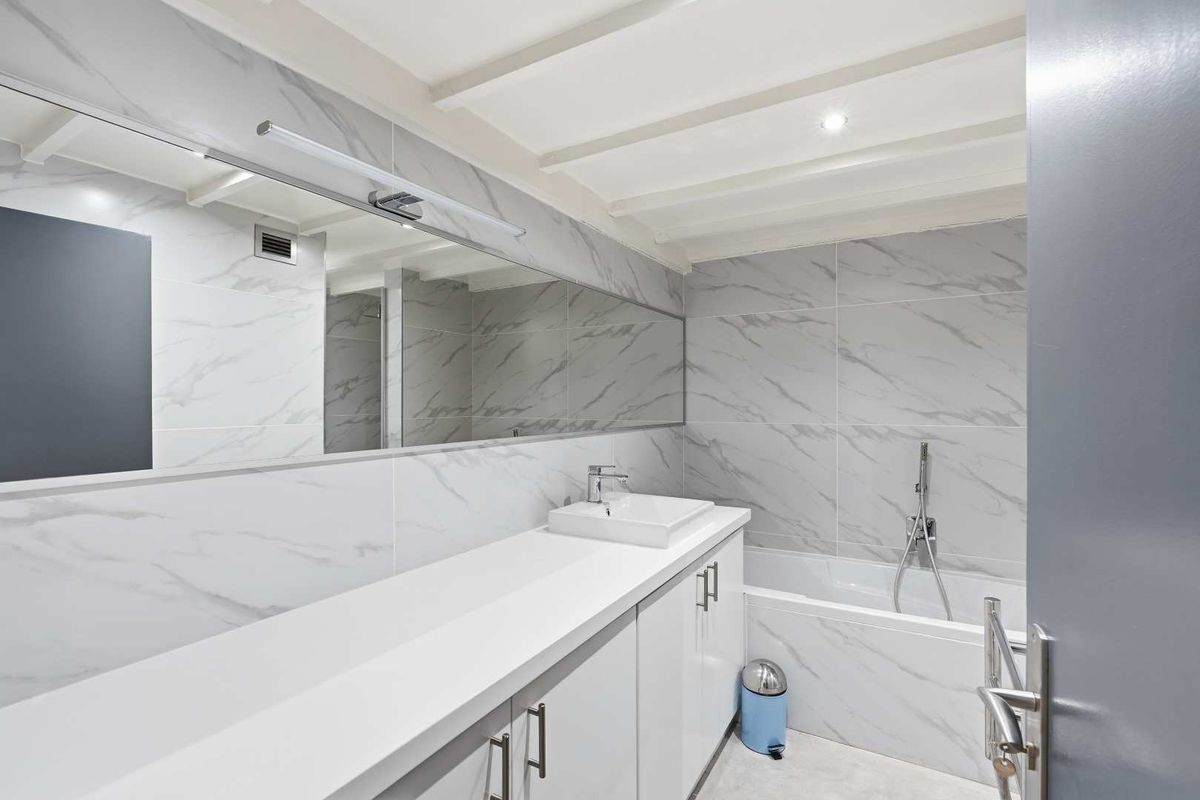 Modern bathroom featuring marble-look wall tiles, a sleek built-in vanity with a countertop basin, a large mirror, and a bathtub with a handheld shower.