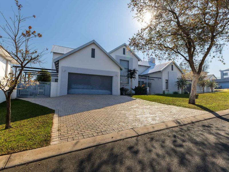 A well-maintained modern house featuring a paved driveway, double garage, and neat front lawn with established trees.