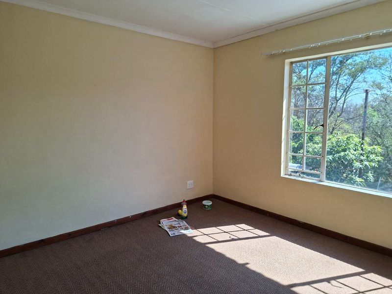 A vacant bedroom featuring neutral walls, carpeted flooring, and a large window providing natural light and garden views.