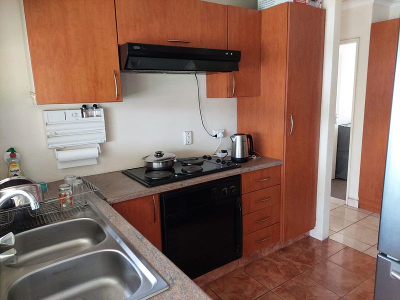 A functional kitchen featuring wood-look laminate cabinetry, a built-in oven and hob, extractor fan, and a double bowl stainless steel sink.