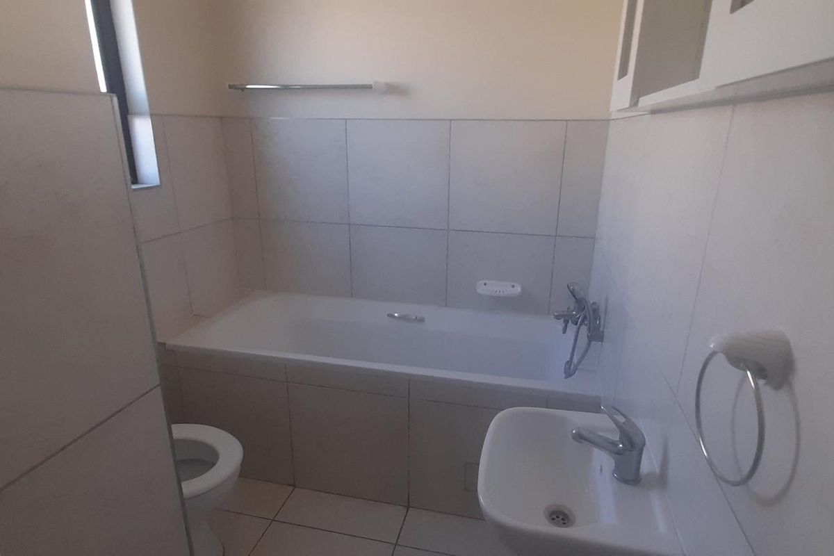 A functional bathroom featuring a built-in bathtub, wall-mounted basin, and toilet with neutral wall and floor tiling.