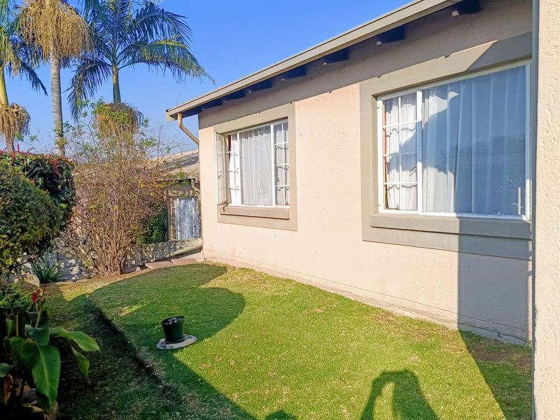 A view of the rear exterior of the townhouse featuring a small lawn area and plastered walls with sliding windows.