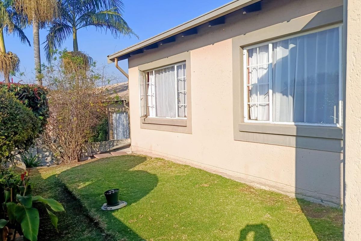 A view of the rear exterior of the townhouse featuring a small lawn area and plastered walls with sliding windows.