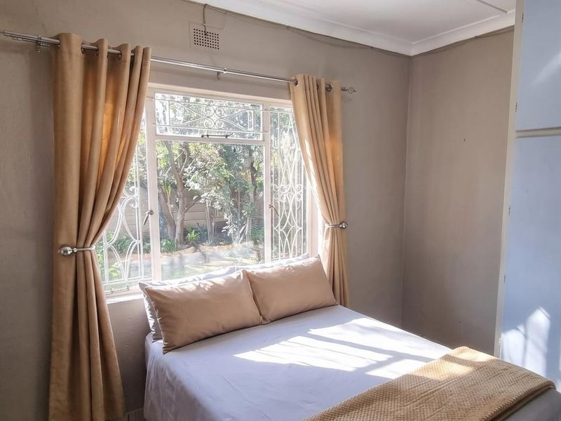 A compact bedroom featuring built-in cupboards and security bars on the window, requiring some cosmetic updates to the walls and ceiling.