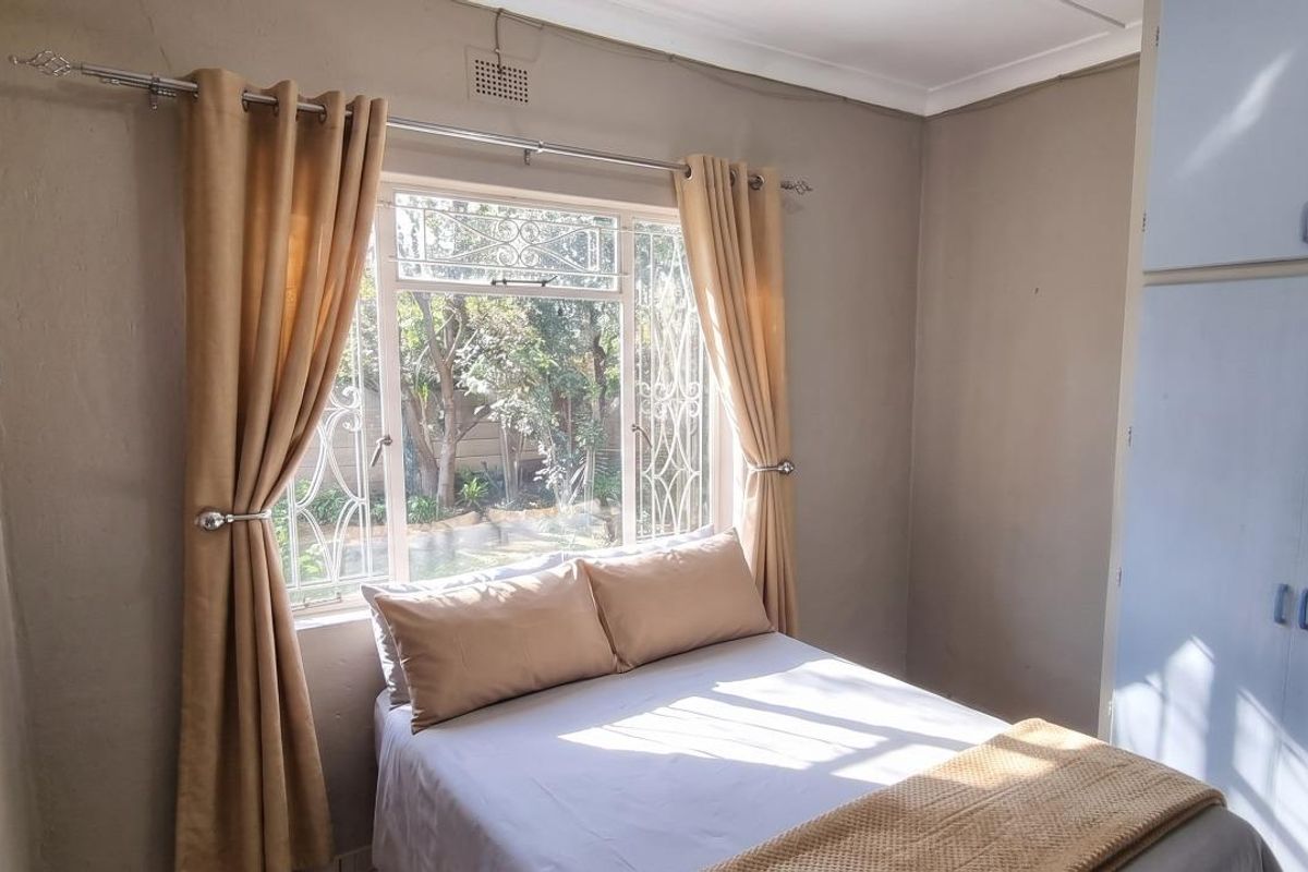 A compact bedroom featuring built-in cupboards and security bars on the window, requiring some cosmetic updates to the walls and ceiling.