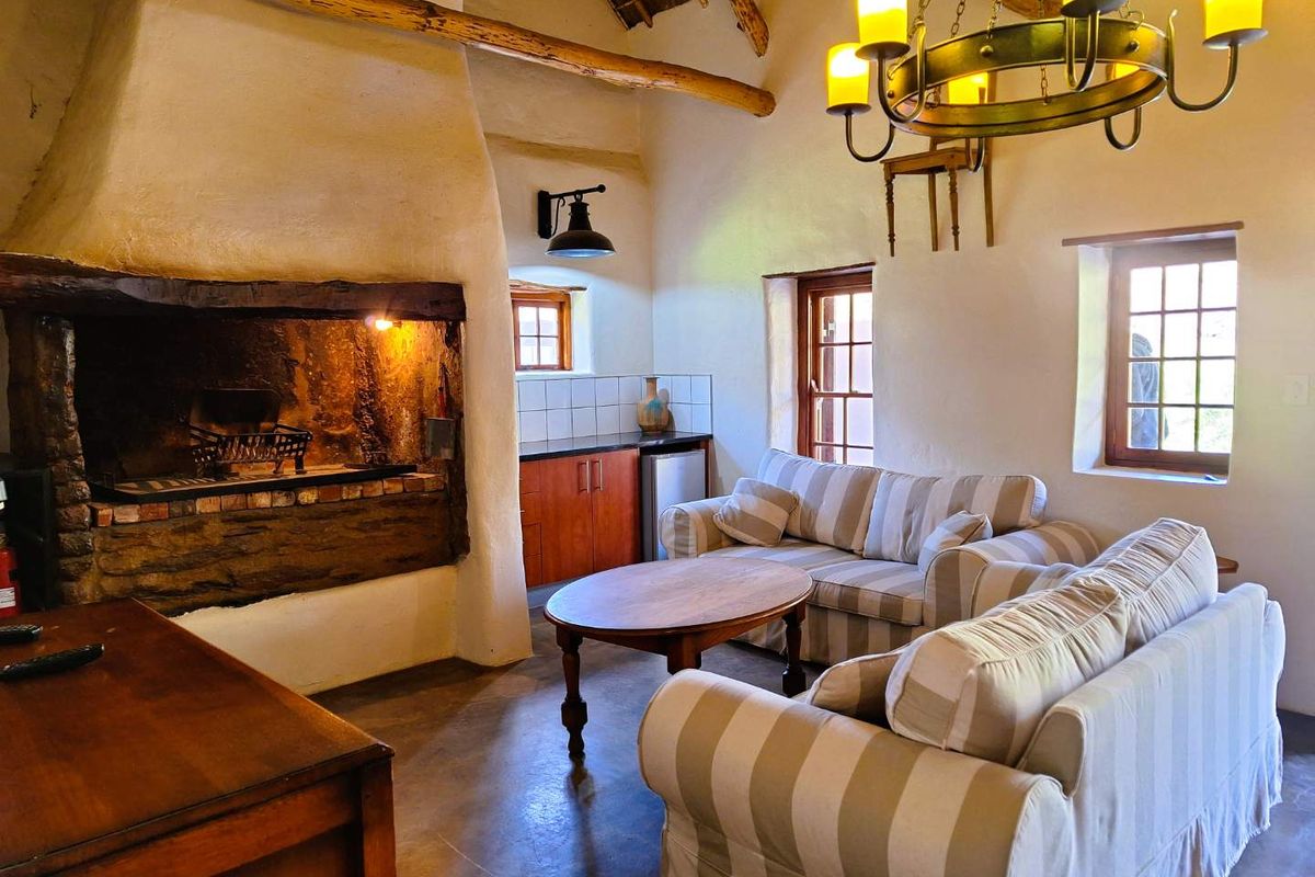 Rustic living room featuring a large stone fireplace, exposed timber beams, thatched ceiling, and integrated cabinetry with a tiled backsplash.