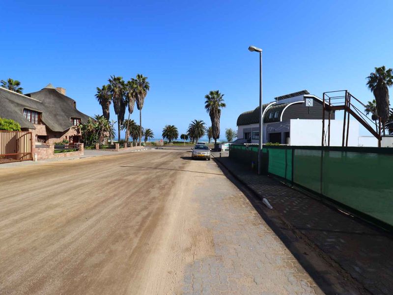 A street view showing the residential road approach with surrounding properties, palm trees, and clear coastal sky.