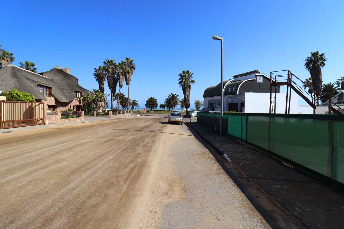 A street view showing the residential road approach with surrounding properties, palm trees, and clear coastal sky.