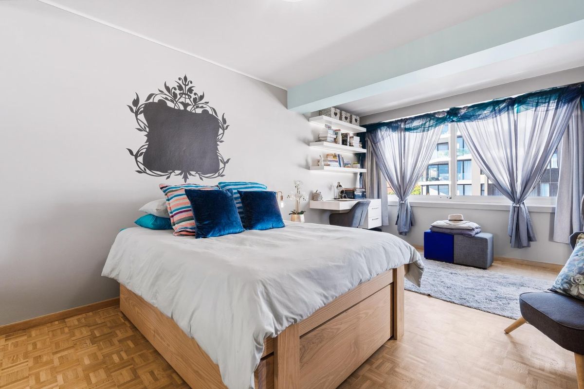 A well-lit bedroom featuring parquet flooring, built-in shelving, and a dedicated desk area, offering a functional and comfortable living space.
