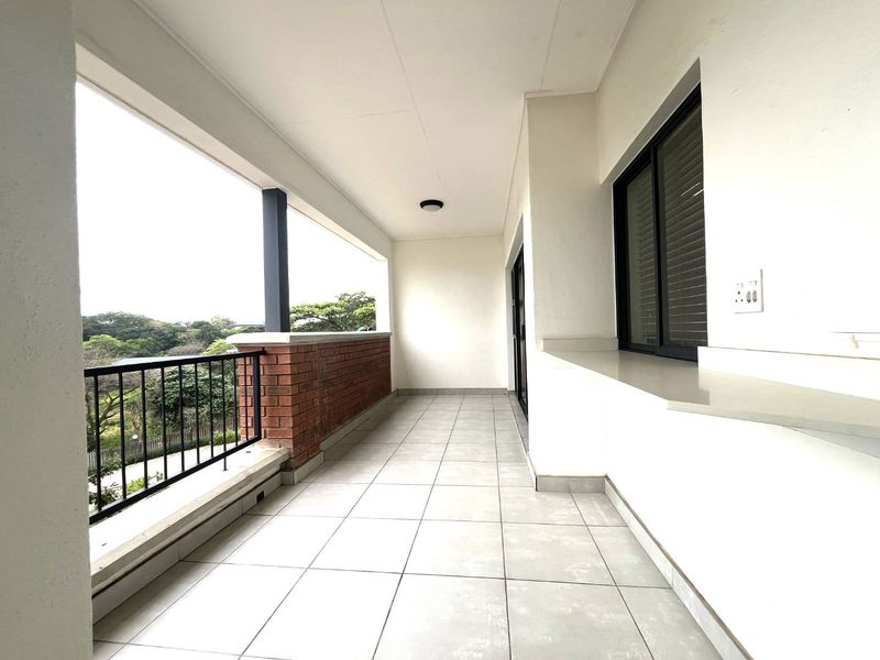 A spacious, covered balcony featuring tiled flooring, a brick balustrade with metal railing, and a built-in counter, offering a clean and functional outdoor living space.