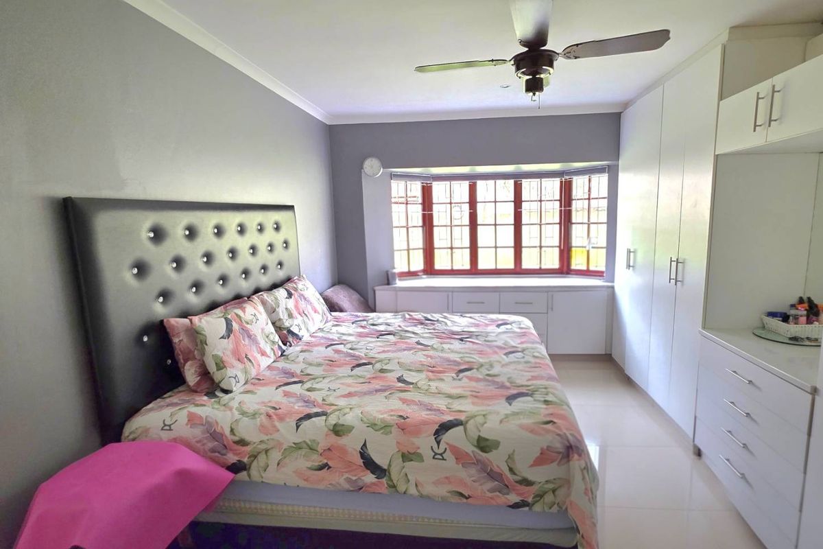 Spacious bedroom featuring built-in cupboards, a bay window with integrated storage, tiled flooring, and a ceiling fan.