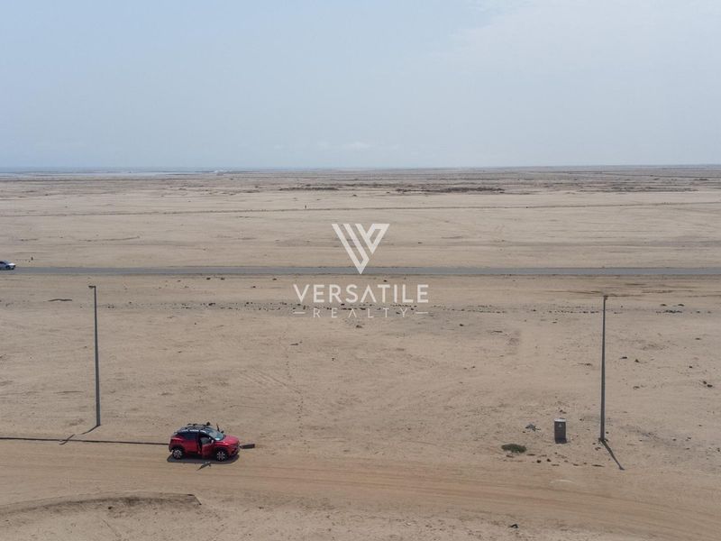 An aerial view of a large, flat, vacant residential plot featuring basic utility infrastructure and road access.