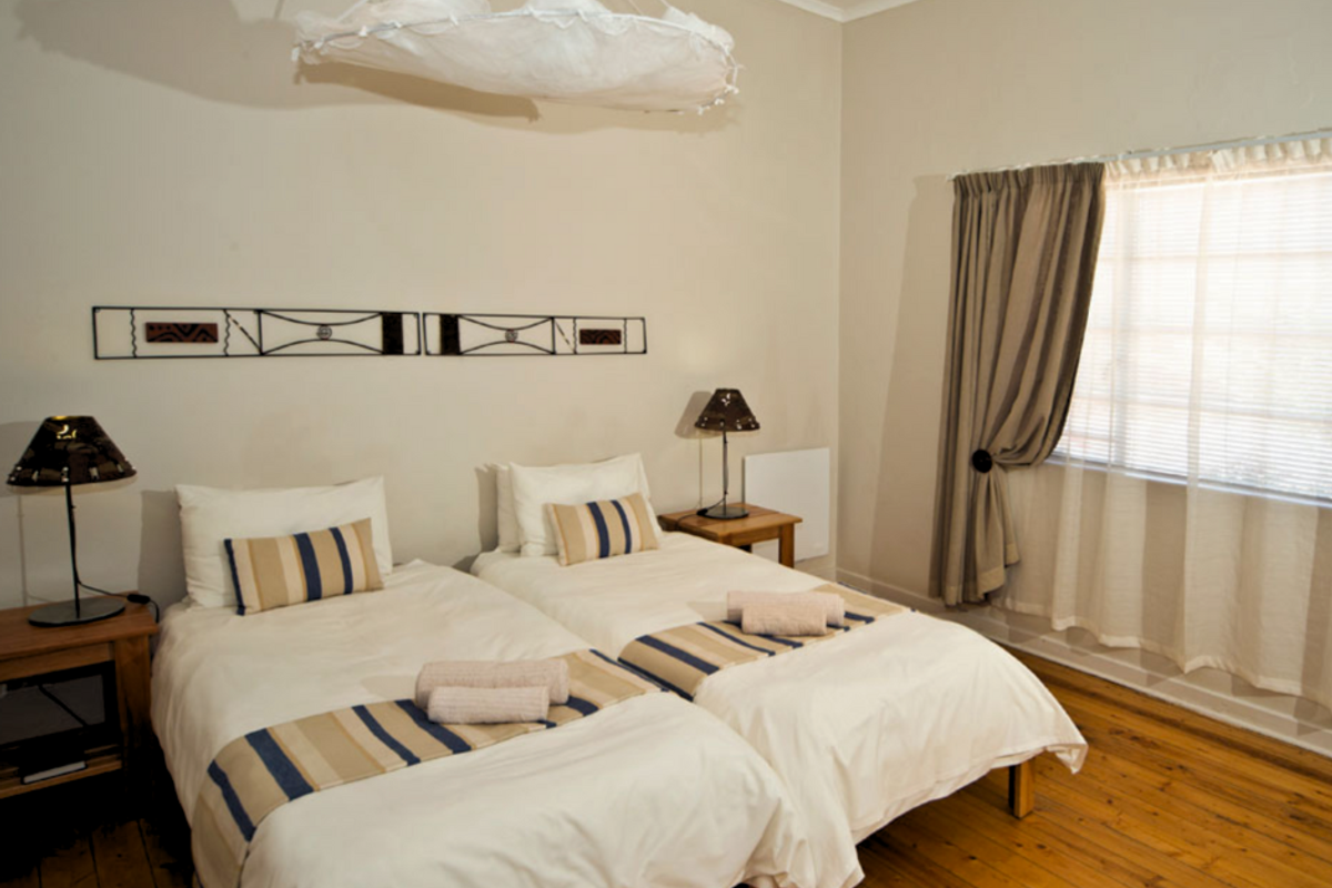 A hotel bedroom featuring twin beds, wooden flooring, and a window with curtains, providing a functional and comfortable space for guests.