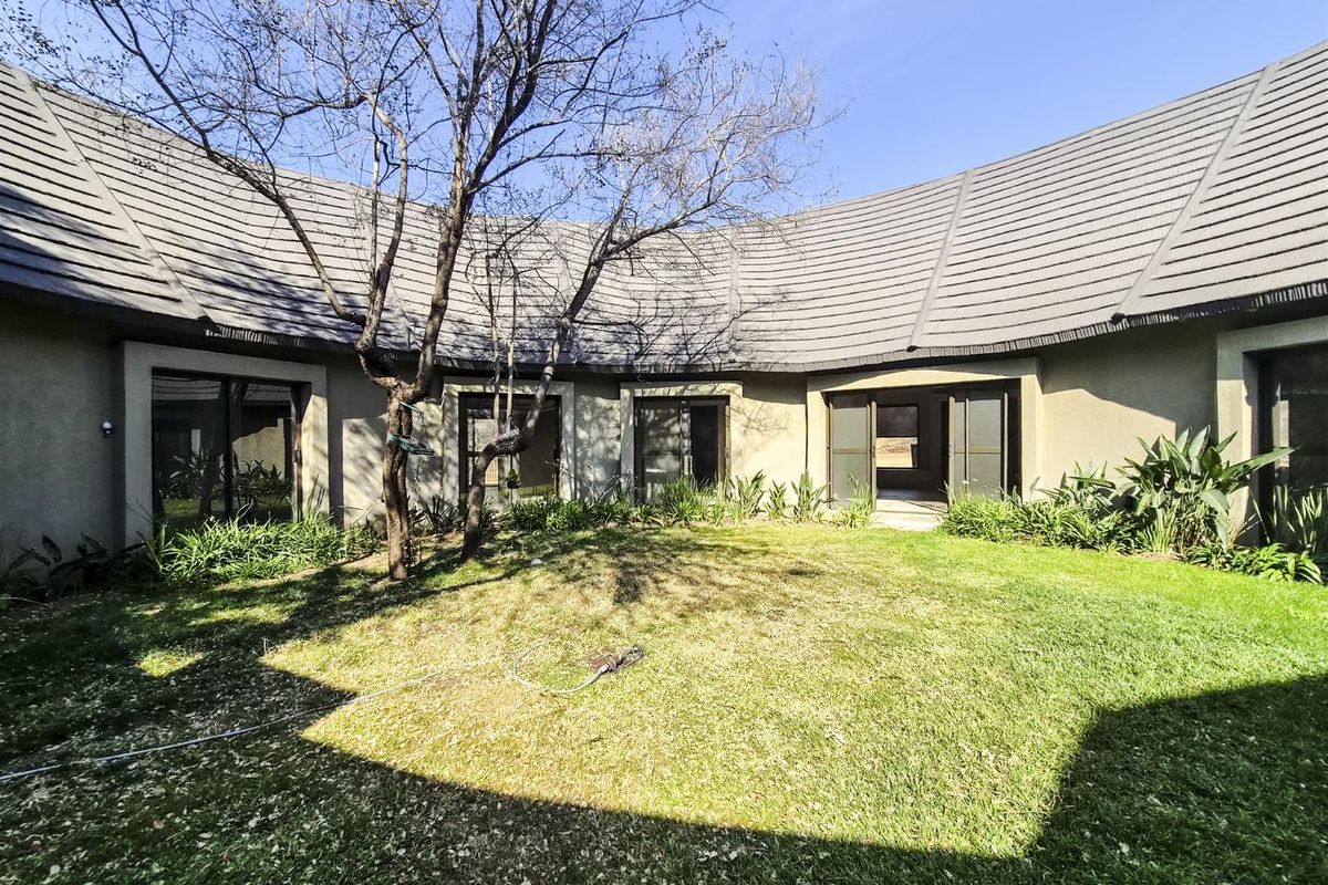 A view of the rear exterior of the house featuring a curved roofline, landscaped garden, and multiple sliding glass door access points.