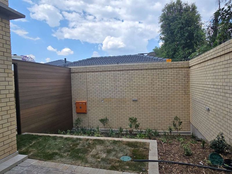 A private rear courtyard featuring a brick boundary wall, timber privacy screen, paved patio area, and a small landscaped garden bed.