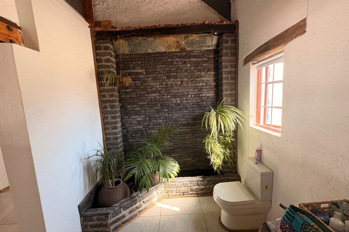 A unique bathroom featuring a stone accent wall, exposed timber beams, and tiled flooring, creating a rustic and textured aesthetic.