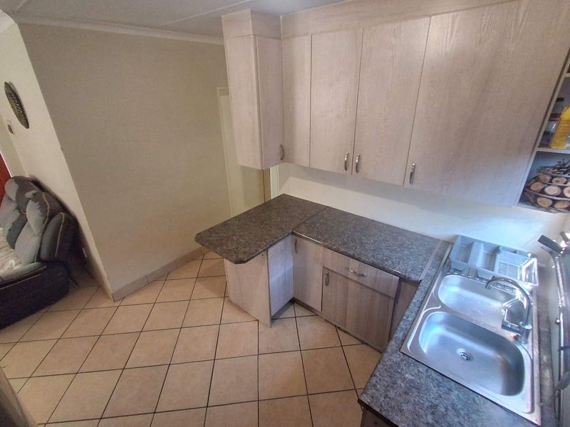 A functional kitchen area featuring light wood-tone cabinetry, dark laminate countertops, and a double stainless steel sink with tiled flooring.