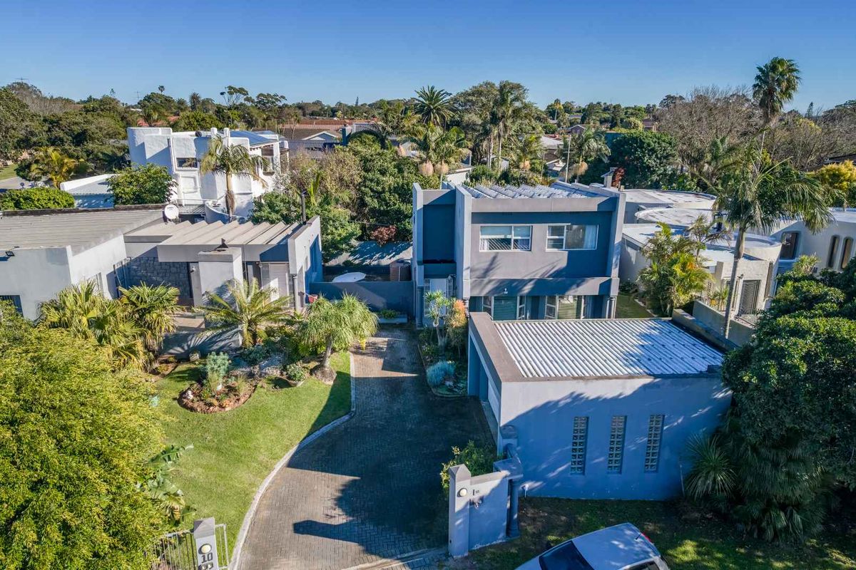 Aerial view of a modern multi-level residential property featuring a paved driveway, flat roof with solar panels, and established garden landscaping.