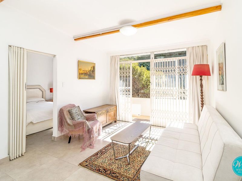 Bright living room featuring tiled floors, a folding door leading to the bedroom, and sliding glass doors with security gates opening to the outdoors.
