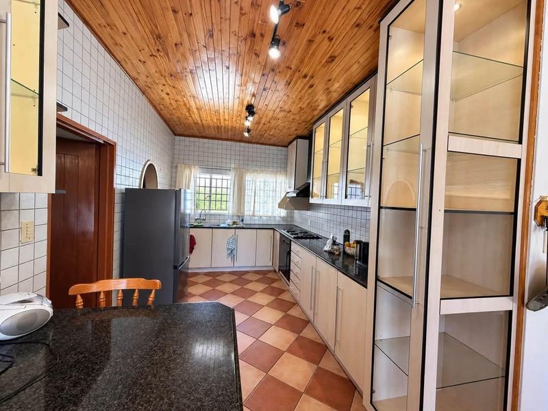 A functional kitchen featuring granite countertops, built-in cabinetry, glass display units, and a distinctive timber ceiling, offering a classic layout with ample storage space.